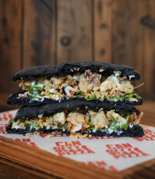 Focaccia de calamares: la base es la clásica masa de larga fermentación con tinta de calamar, sobre la que se asientan calamares fritos, stracciatella de burrata, pesto de tomate seco, rúcula y un alioli fino. Foto: agencia.